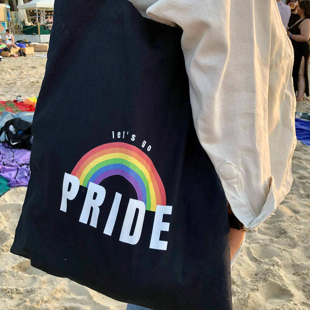 Person trägt dunkelblauen Jutebeutel mit einem Regenbogen und der Aufschrift let's go Pride