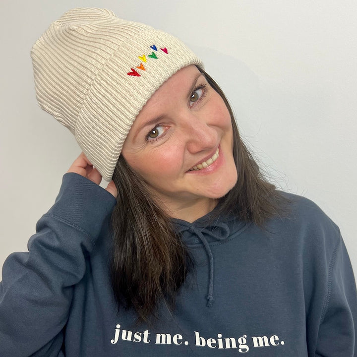 Person trägt Organic Beanie natur mit Regenbogenherzen Stick