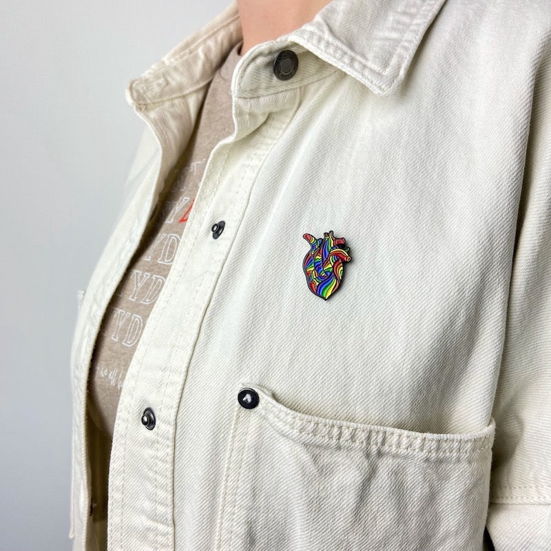 Anstecknadel menschliches Herz in Regenbogenfarben ist an eine Jacke gepinnt