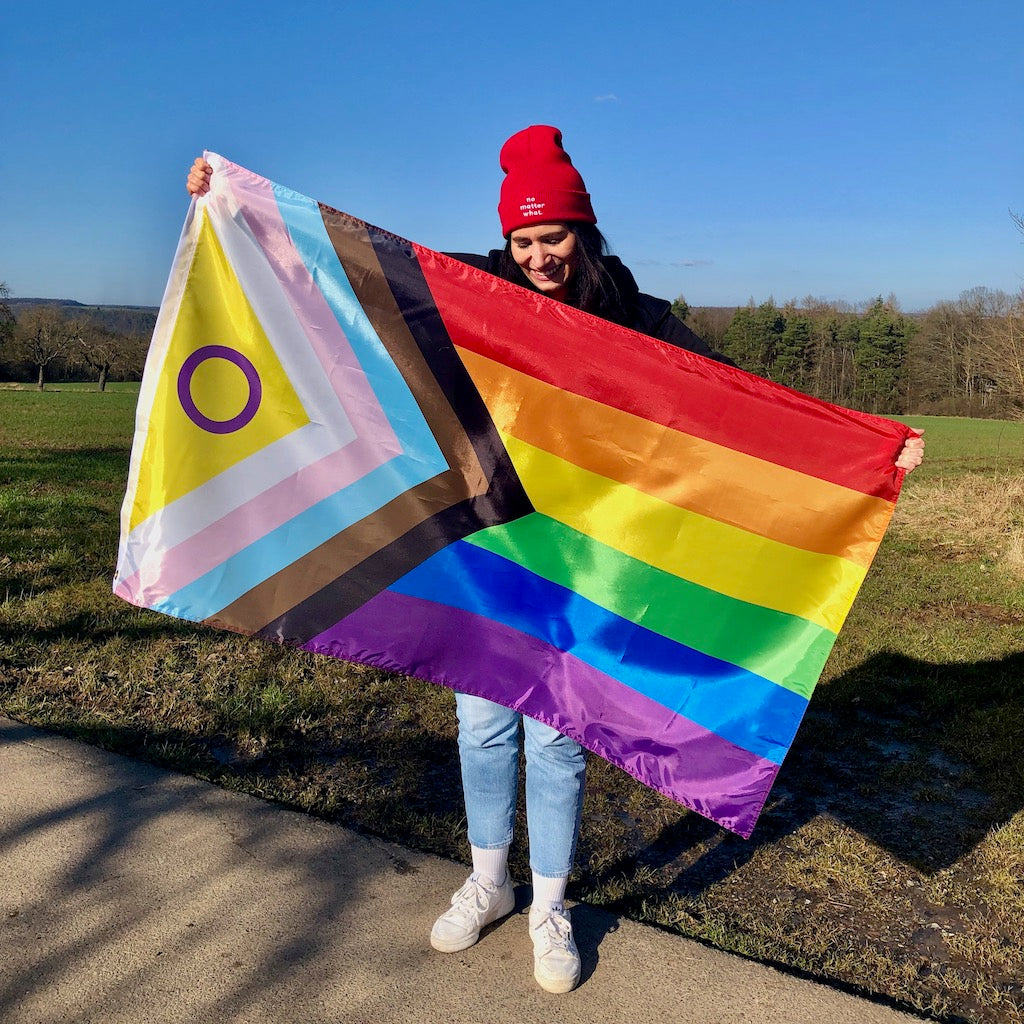 Person hält die Progress Pride Flag in den Händen und lächelt