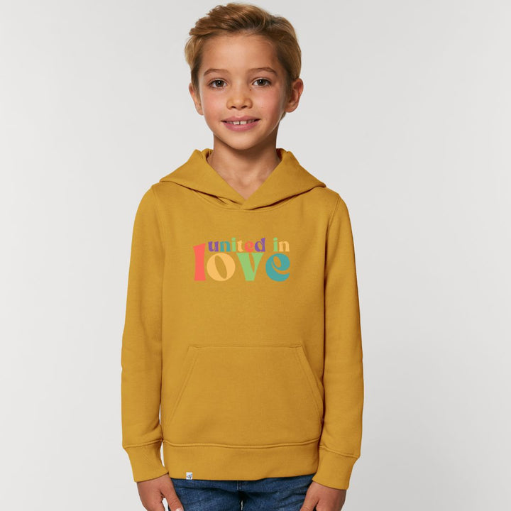 Kind lächelt und trägt Hoodie in der Farbe Ocker mit dem Aufdruck united in love