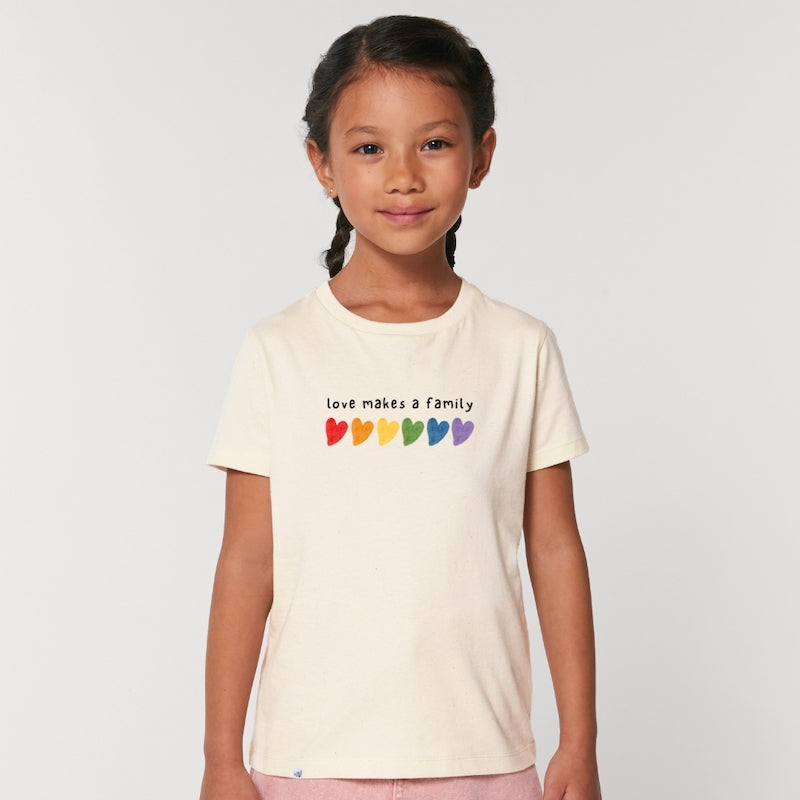Kind lächelt in die Kamera und trägt naturfarbenes Shirt mit dem Aufdruck love makes a family und bunten Herzen
