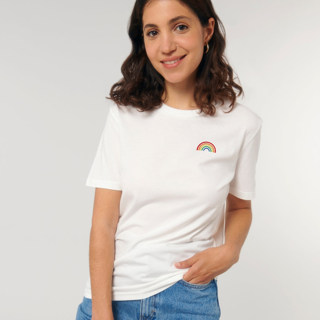 Person lächelt und trägt Shirt in der Farbe off white mit gesticktem Regenbogen auf der Brust