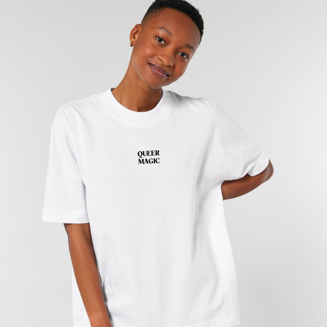 Person lächelt und trägt weißes oversized Shirt mit dem Aufdruck Queer Magic