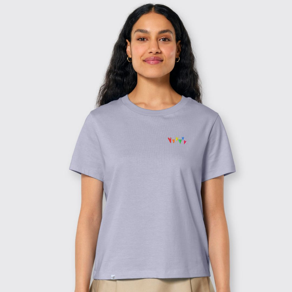 Model lächelt und trägt lavendelfarbenes Shirt mit kleinen gestickten Herzen in Regenbogenfarben