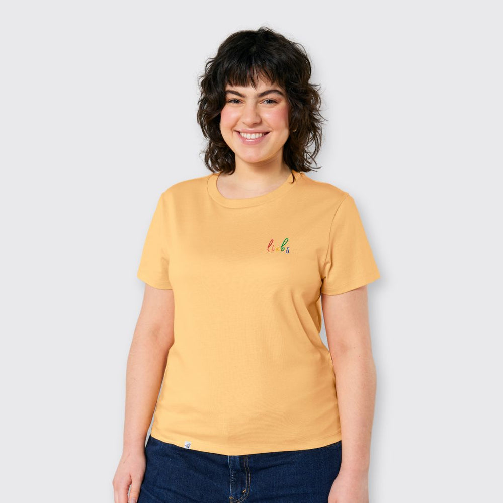 Model lächelt und trägt Shirt in Sonnengelb mit kleinem Stick liebs in Regenbogenfarben