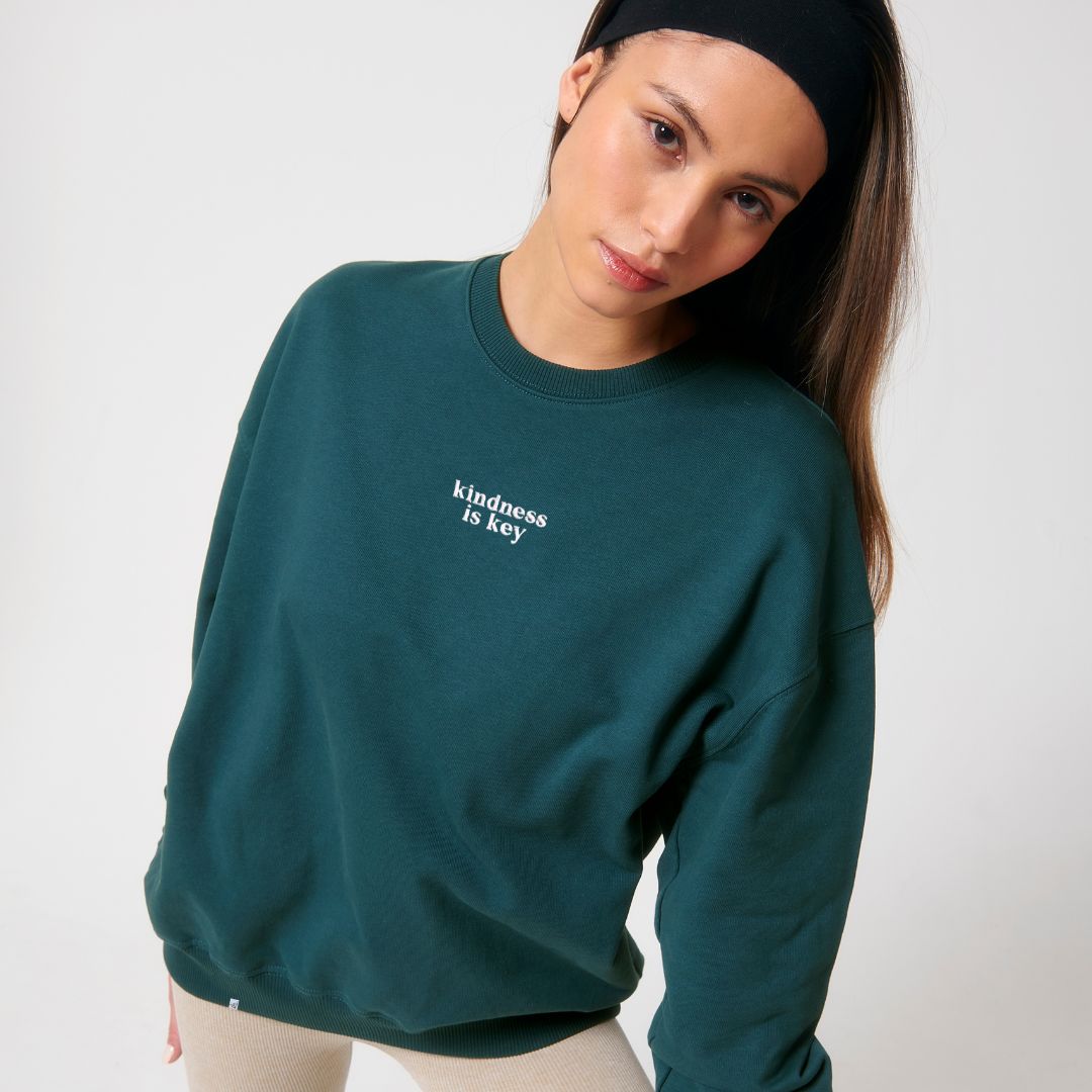 Model trägt petrolgrünes oversized Sweatshirt mit weißem Stick kindness is key
