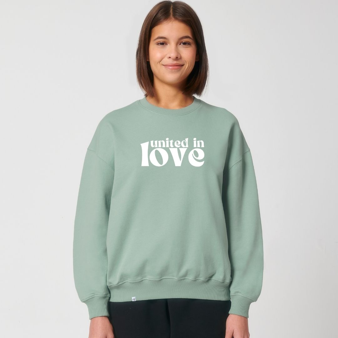 Model lächelt und trägt Sweatshirt in der Farbe Aloe mit dem Aufdruck united in love