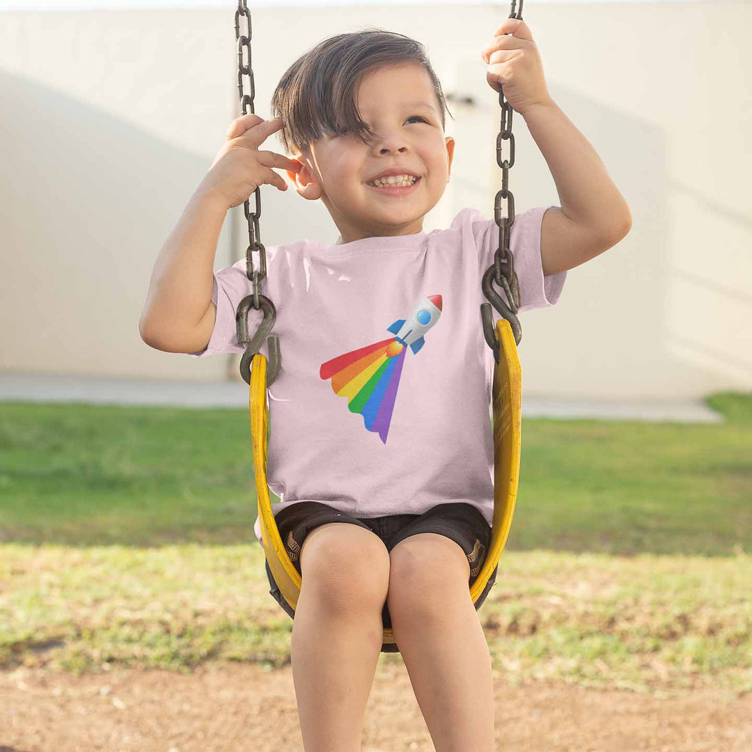 Kind sitzt auf einer Schaukel und trägt ein petrolfarbenes Shirt mit einer Rakete mit Regenbogenschweif
