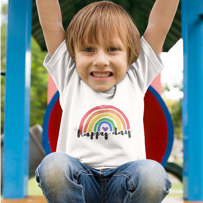 Kind lächelt und trägt ein weißes Shirt mit einem Regenbogen und der Aufschrift happy day