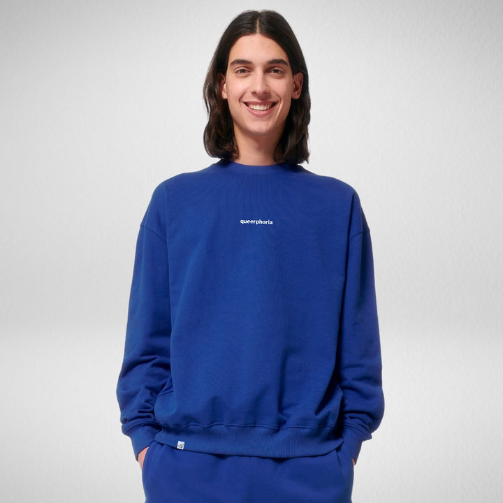 Person lächelt in die Kamera und trägt ein Oversized Sweatshirt in der Farbe Marine Blau mit dem Stick queerphoria