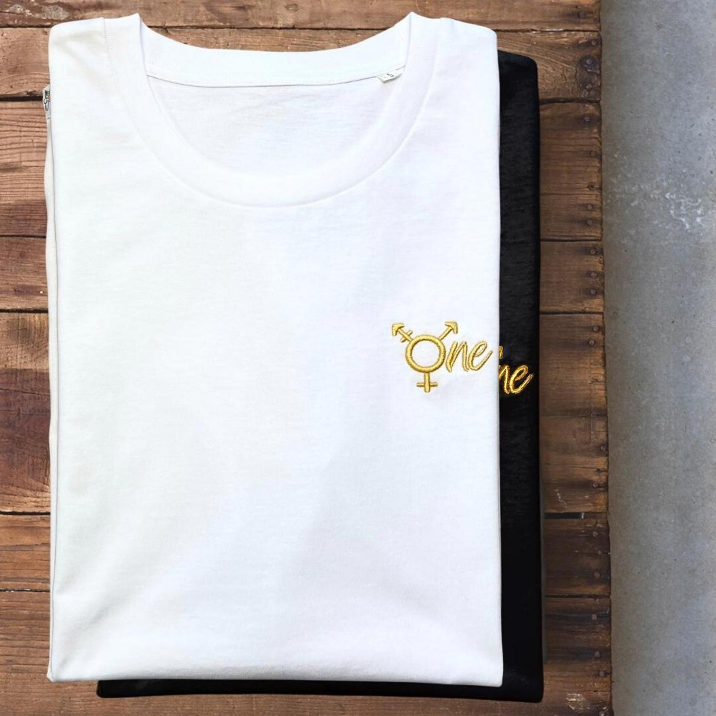 Schwarzes und weißes Shirt mit dem All Gender Symbol ONE in goldenem Stick
