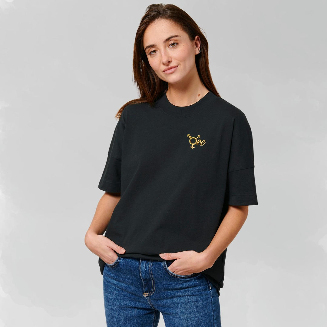 Model trägt schwarzes oversized Shirt mit dem All Gender Symbol ONE in goldenem Stick