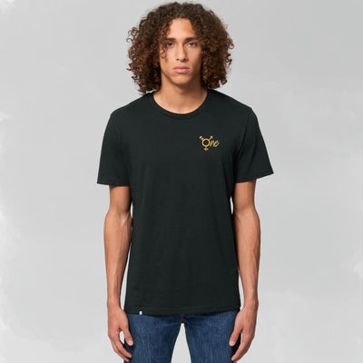 Model trägt schwarzes Shirt mit geradem Schnitt mit dem All Gender Symbol ONE in goldenem Stick