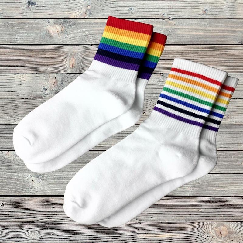 Zwei Paar Socken mit Streifen in Regenbogenfarben liegen auf einem Holztisch
