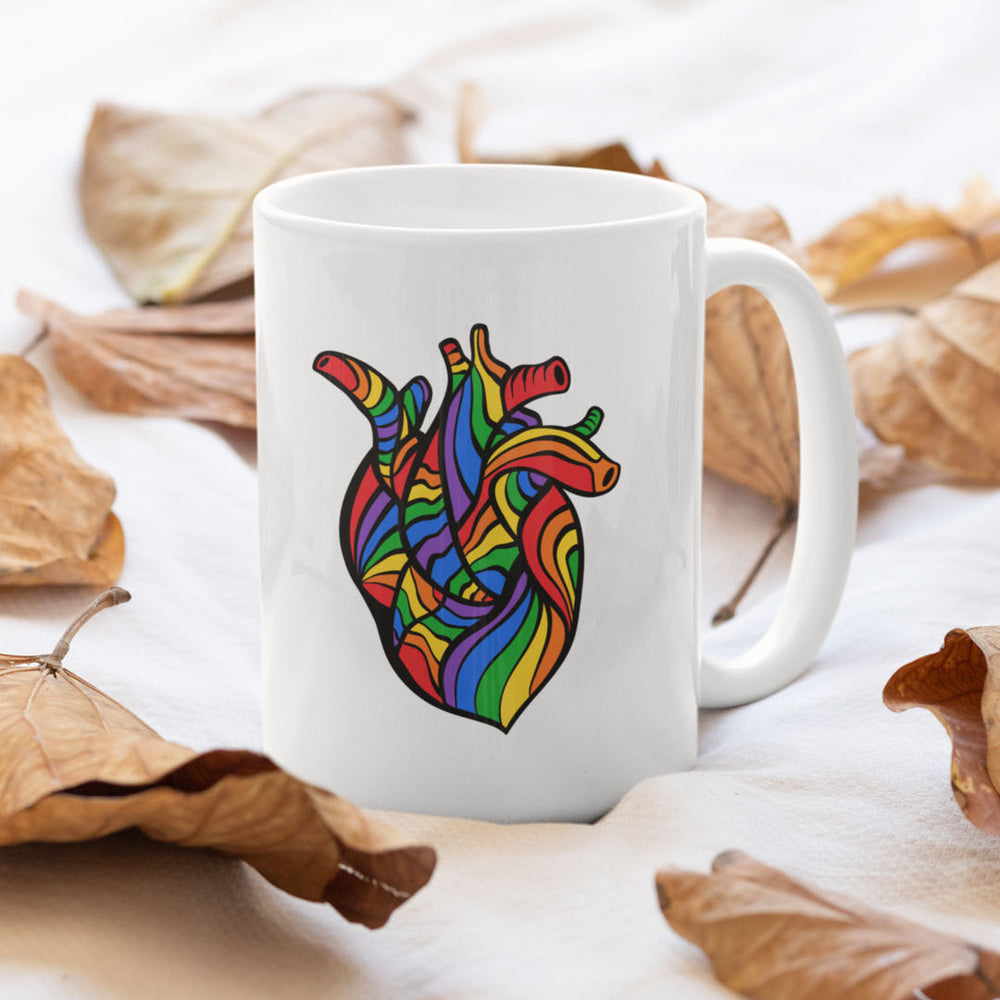 Weiße Tasse mit einem menschlichen Herz in Regenbogenfarben inmitten von Herbstlaub